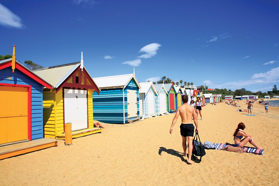 Sun bathers enjoying Brighton Beach with the iconic Brighton Beach Boxes in the background